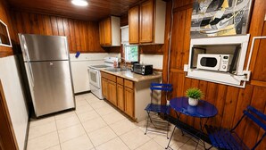 A compact kitchen with wooden cabinets, a stainless steel refrigerator, a microwave, and a small dining area with blue chairs and a table. - Cozy Florida Stay in Bradenton (Bradenton)