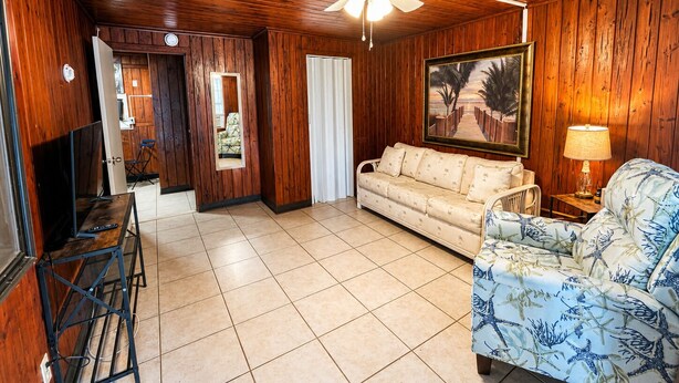 A room with wooden walls and ceiling, a ceiling fan, a sofa, a chair, a television, and a framed picture. - Cozy Florida Stay in Bradenton (Bradenton)