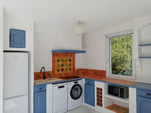 Eine kompakte Küche mit Waschmaschine, Mikrowelle und einem Fenster mit Blick auf Grünflächen.