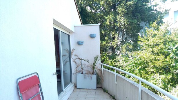 En balkon med en potteplante, en rød stol og et vindue.