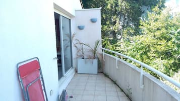 A balcony with a potted plant, a red chair, and a window.