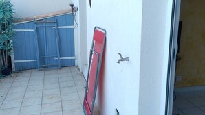En fliseterrasse med et blåt gelænder, en rød foldestol og en vandhane på væggen.