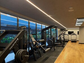 A gym with various exercise equipment, large windows, and a wooden floor.