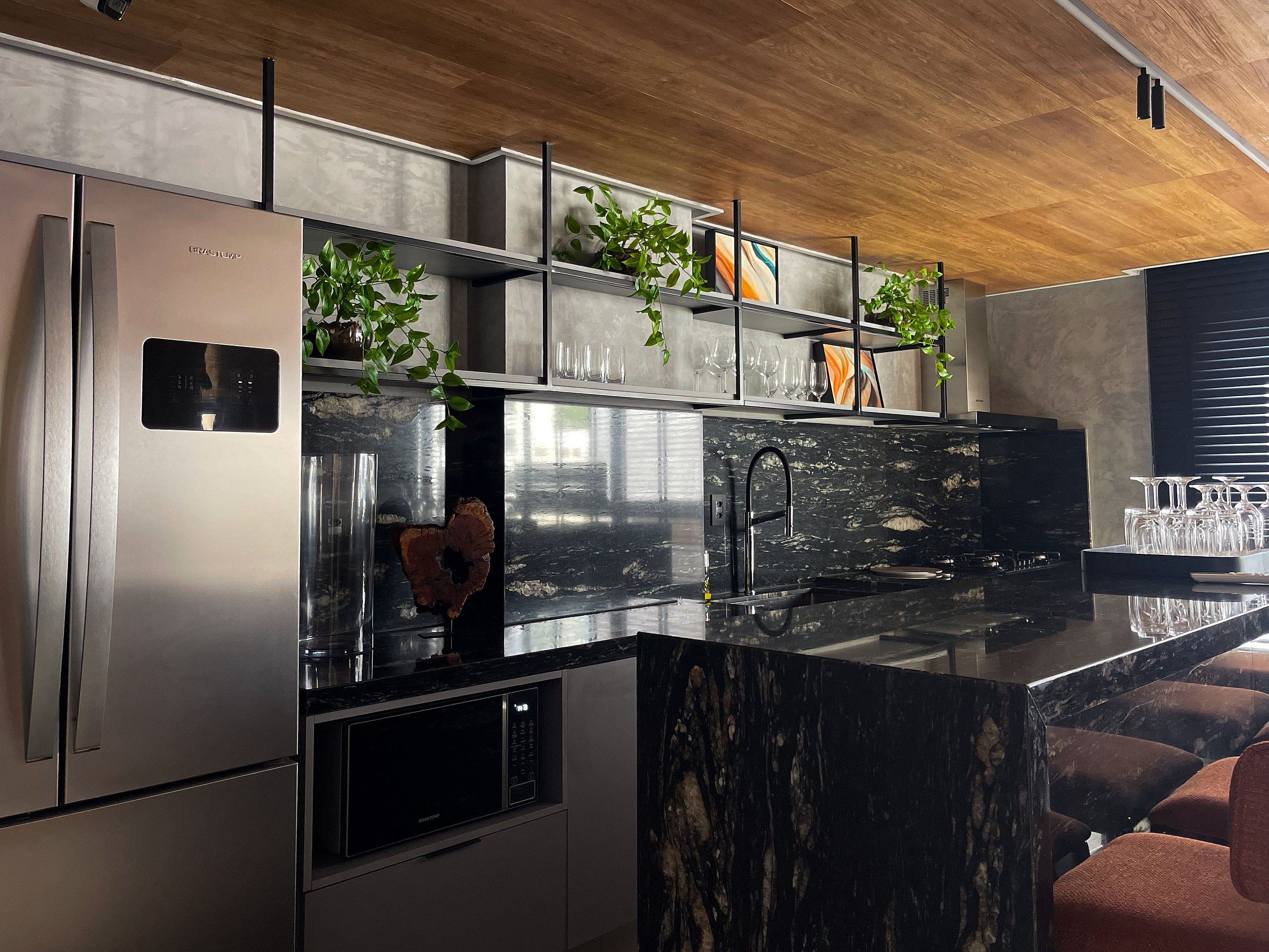 Cozinha moderna com eletrodomésticos de aço inoxidável, bancada de mármore preto e forno embutido.