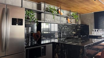 Cozinha moderna com eletrodomésticos de aço inoxidável, bancada de mármore preto e forno embutido.