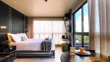 A modern hotel room with a large bed, a seating area with a table, and a view of the outdoors through large windows.