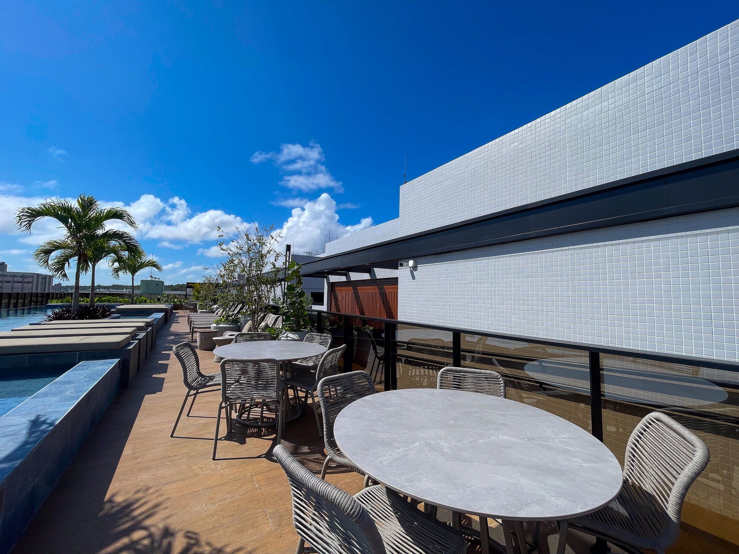 Área externa com mesas, cadeiras, piscina e vista do céu.