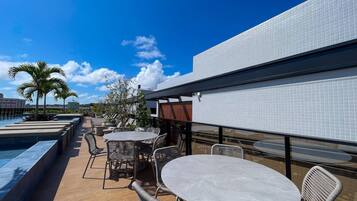 Área externa com mesas, cadeiras, piscina e vista do céu.