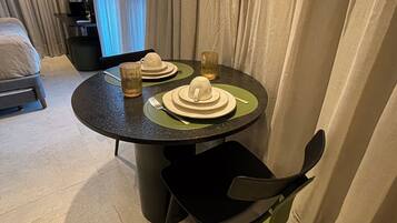 Mesa de jantar posta com pratos, copos e talheres, uma cadeira e uma cama ao fundo.