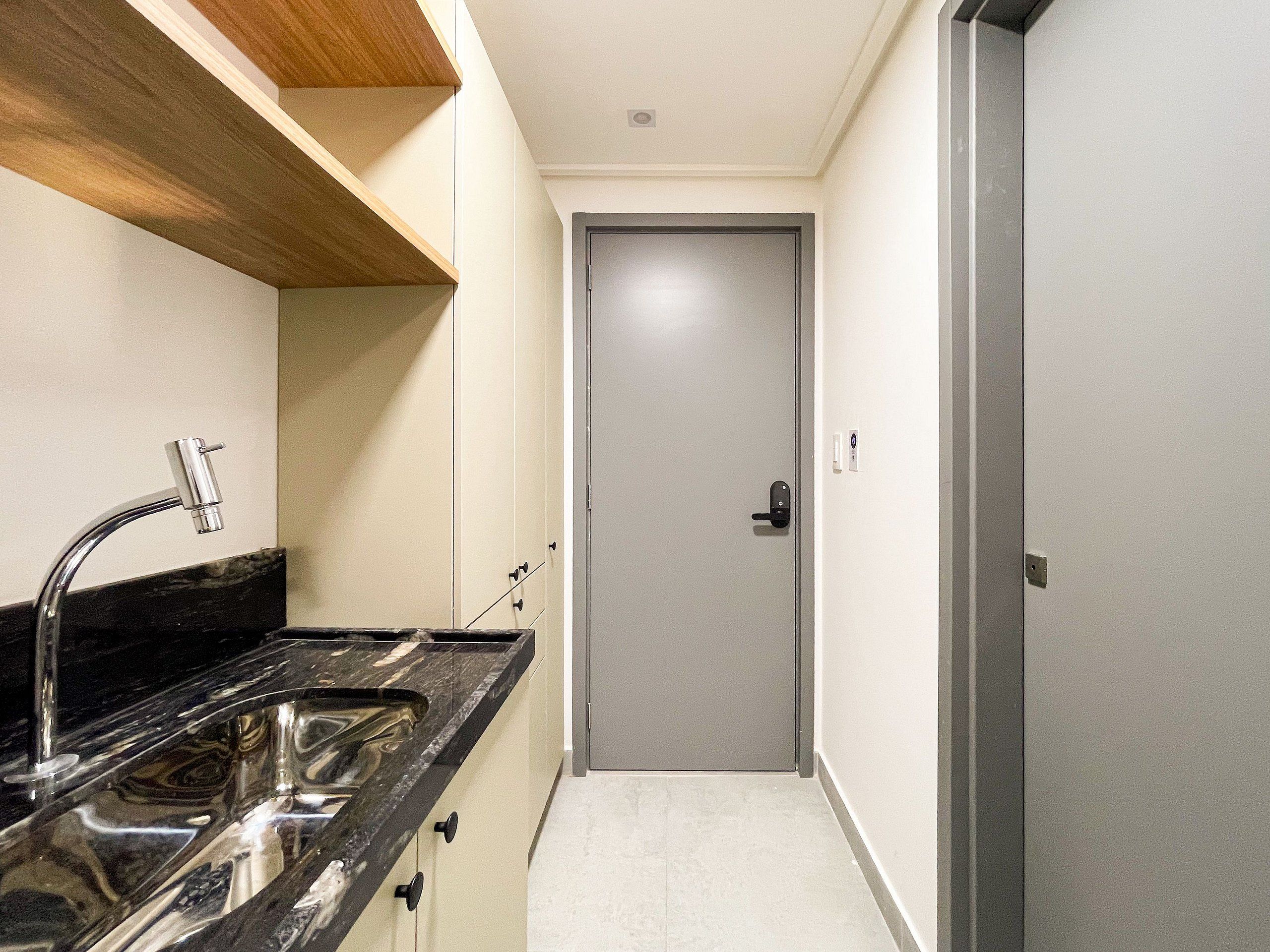 A narrow hallway with a kitchen area on one side, featuring a sink and cabinets.