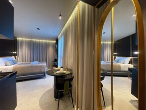 A modern hotel room with a large bed, a small dining table, and a mirror reflecting the room.
