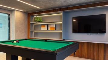 Una mesa de billar con bolas, un televisor y estantes con objetos decorativos.