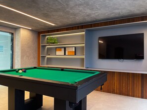 A pool table with balls, a television, and shelves with decorative items.