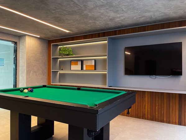A pool table with balls, a television, and shelves with decorative items.