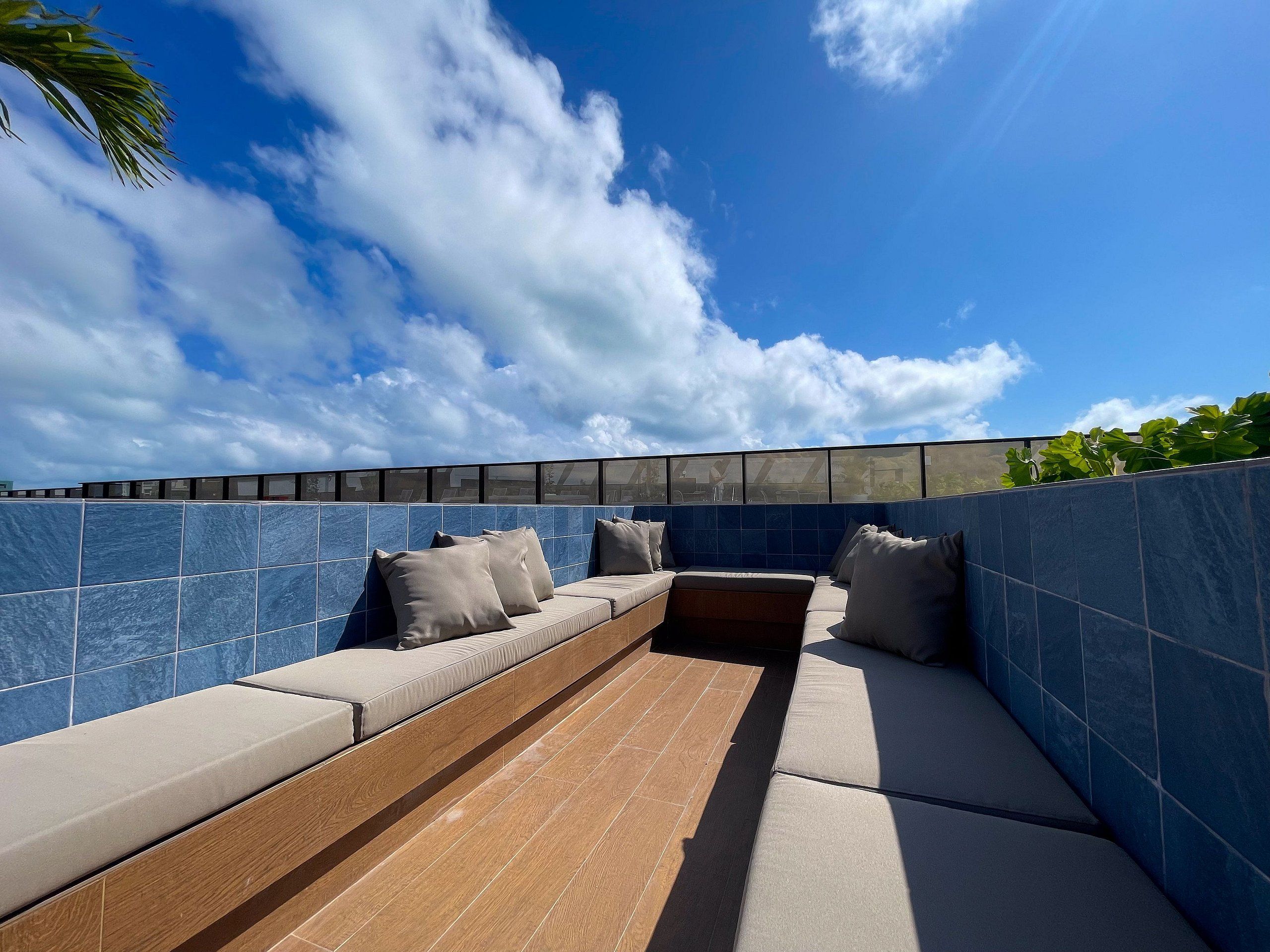 Un espacio al aire libre con sillones y cojines, suelo de madera y pared de azulejos.