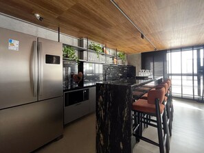 A modern kitchen with stainless steel appliances, a marble island, and a seating area with chairs.