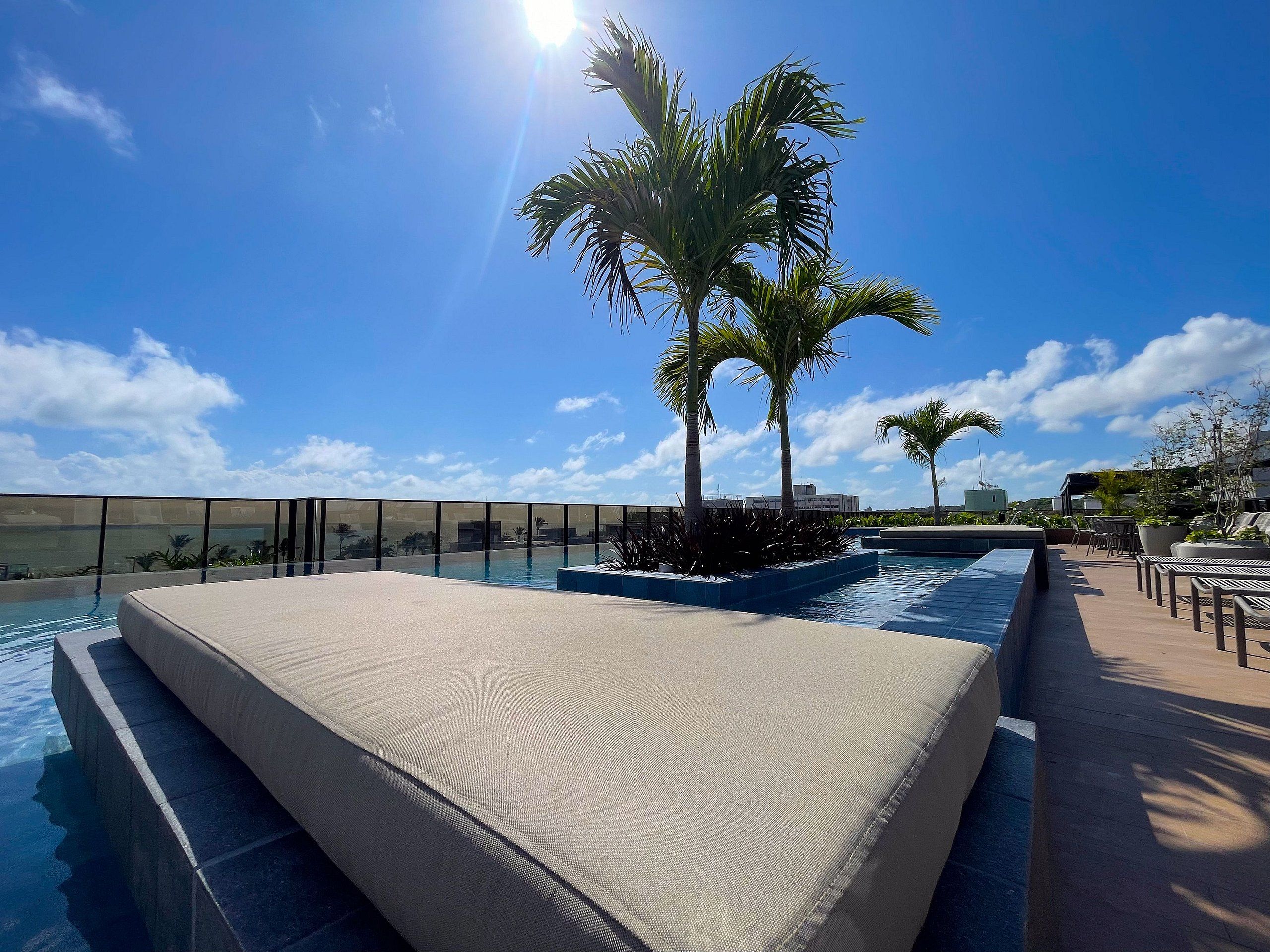 Un área de piscina con una zona de estar hundida, palmeras y cielo despejado.