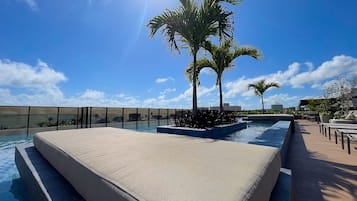 Un área de piscina con una zona de estar hundida, palmeras y cielo despejado.