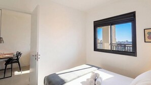 A hotel room with a bed, a window with a city view, a desk with a chair, and a door. - Apt. in Condo. w/ Pool & City View Sru2109 (Campinas)