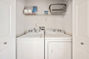 A laundry room with two white Whirlpool washers and dryers, a shelf with laundry supplies, and a basket. - Salt & Sand on Bowfin (Carolina Beach)