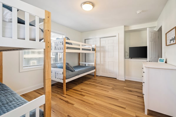 A room with bunk beds, a desk, a television, and a wardrobe. - Salt & Sand on Bowfin (Carolina Beach)