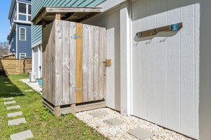 A wooden fence with a metal latch, a concrete stepping stone path, and a white garage door. - Salt & Sand on Bowfin (Carolina Beach)