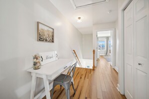 A hallway with a white desk, a chair, and a framed picture on the wall. - Salt & Sand on Bowfin (Carolina Beach)