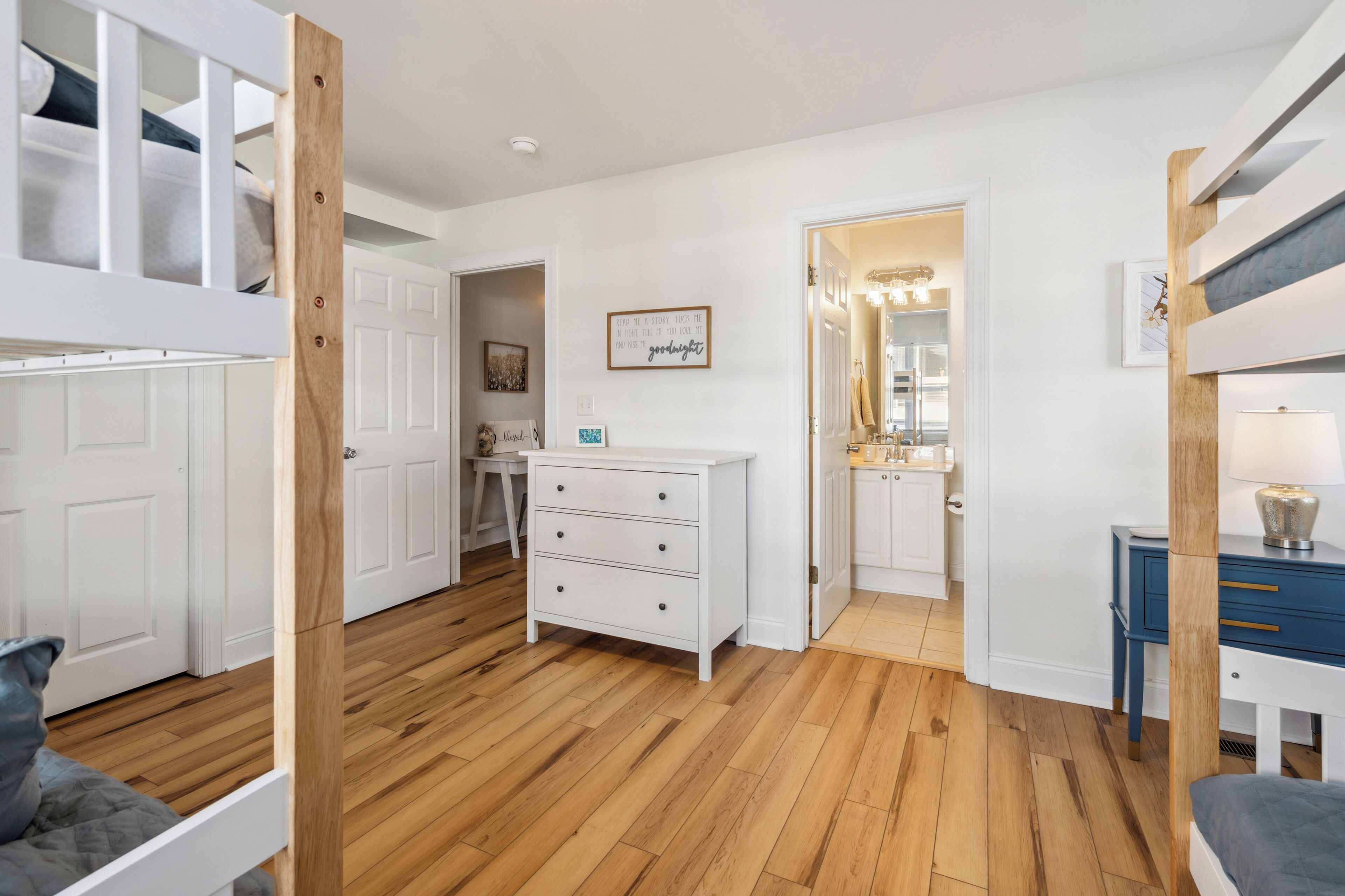 A bedroom with a bunk bed, a dresser, a vanity with a mirror, and a framed quote on the wall.