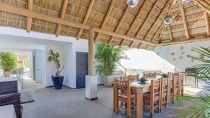 An open-plan dining area with a thatched roof, wooden furniture, and potted plants. - Family oasis near the sea - La Cruz Encantada 2A (La Cruz de Huanacaxtle)