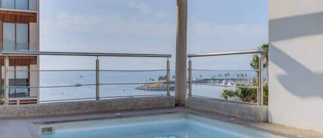 A pool area with a view of the sea and a building with a balcony.