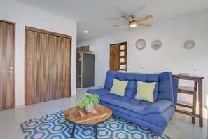 Ein Wohnzimmer mit einem blauen Sofa, einem Holztisch mit einer Pflanze und einem gemusterten Teppich.