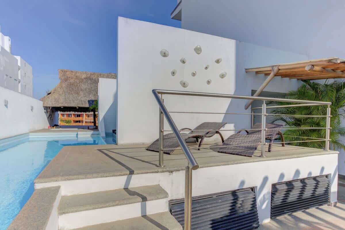 A pool area with steps leading down to the water, lounge chairs, and a pergola structure.