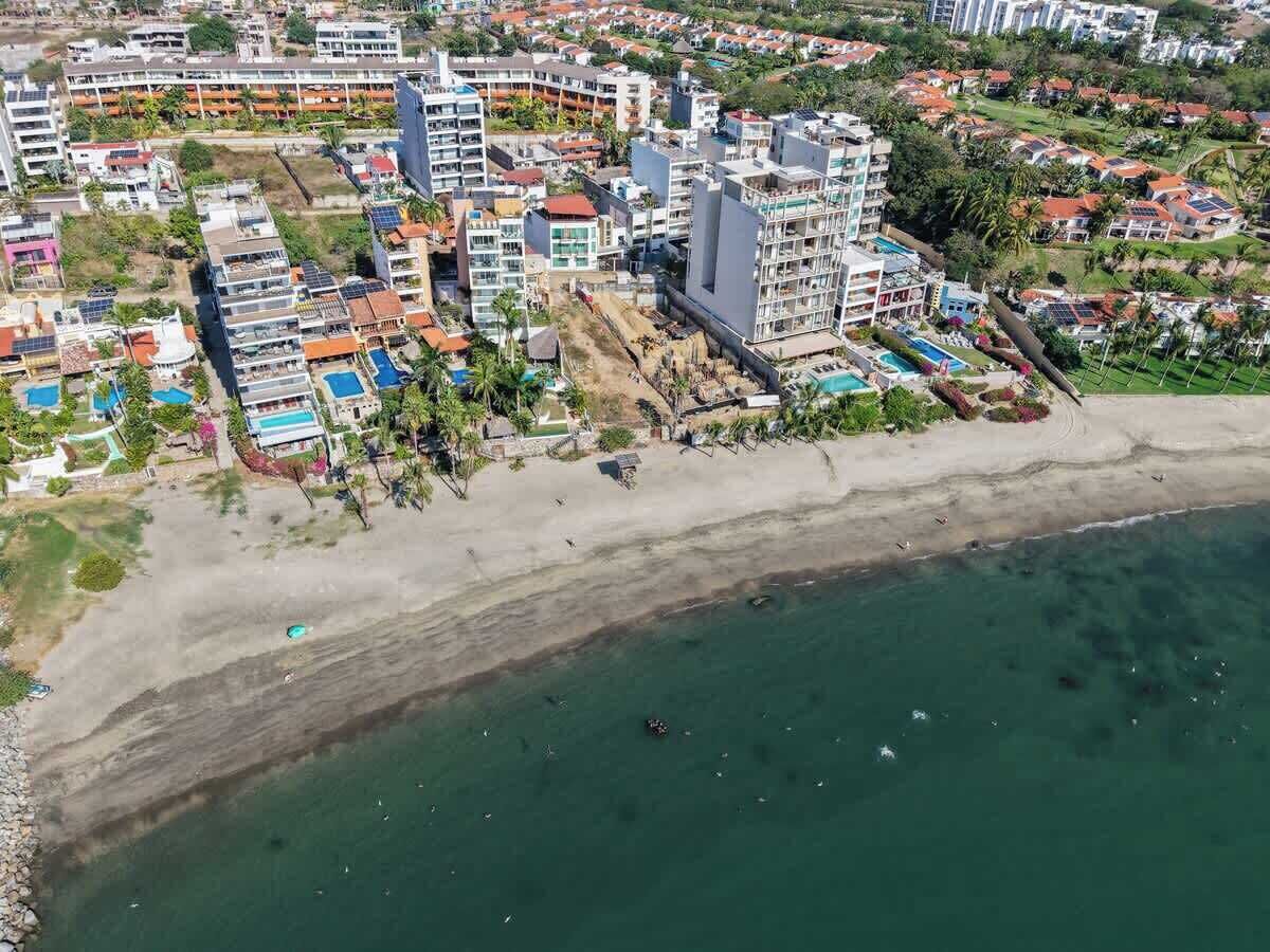 An aerial view of a coastal resort area with multiple buildings, a sandy beach, and a clear view of the ocean.