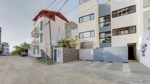 Un edificio residencial de varios pisos con fachada plana, una entrada visible y un pequeño estacionamiento.