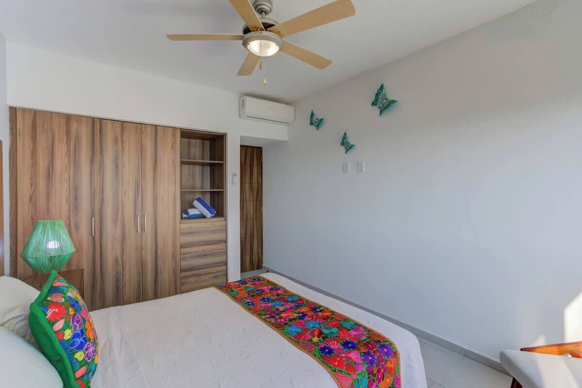 A bedroom with a bed, a ceiling fan, a wardrobe, and a wall-mounted air conditioner.