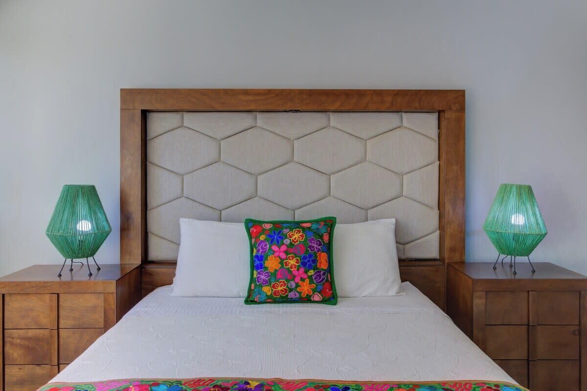 A bed with a wooden headboard, two nightstands, and a colorful decorative pillow.