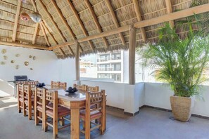A dining area with a thatched roof, wooden furniture, and a large potted plant. - Family oasis near the sea - La Cruz Encantada 3B (La Cruz de Huanacaxtle)