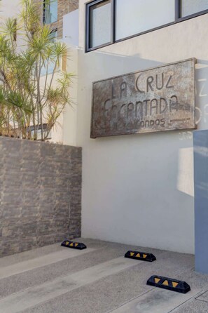 Eine Gebäudefassade mit einem Schild, auf dem 'LA CRUZ GRANADA' steht, und eine Mauer aus Stein mit Pflanzen.
