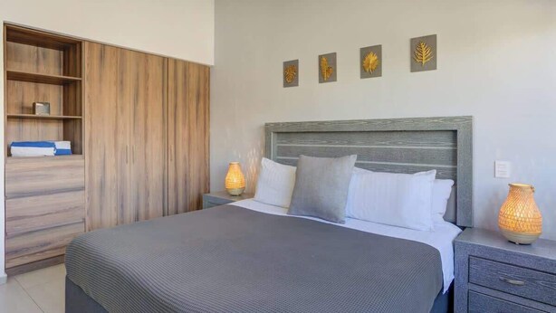 A bedroom with a large bed, a wardrobe, bedside lamps, and wall art. - Family oasis near the sea - La Cruz Encantada 3B (La Cruz de Huanacaxtle)