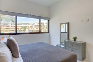 Ein Schlafzimmer mit Bett, Schminktisch, Spiegel und einem Fenster mit Blick auf Gebäude.