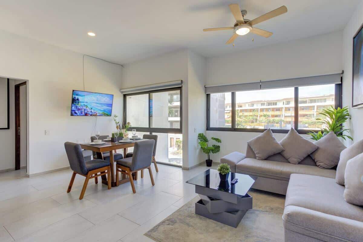 Un salon moderne comprenant un coin repas, un ventilateur de plafond, de grandes fenêtres et une vue sur l’extérieur.