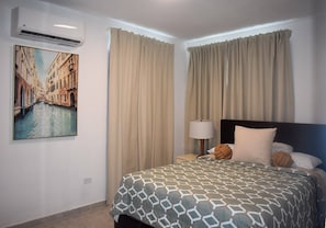 A hotel room with a bed, curtains, a lamp, a pillow, a wall-mounted air conditioner, and a painting of a canal. - Villa Aerio (Carolina)