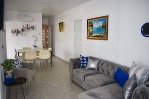 A living room with a grey sofa, a dining table with chairs, a potted plant, and a painting on the wall. - Villa Aerio (Carolina)