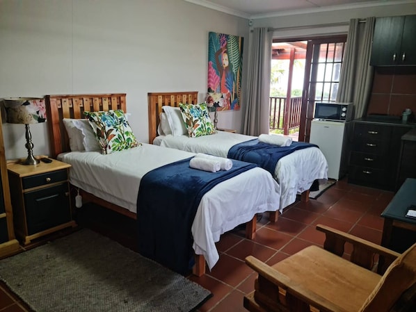 A hotel room with two beds, a desk, a chair, a TV, and a painting on the wall.
