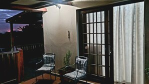 Eine Terrasse mit zwei Stühlen, einem kleinen Tisch und einer Glastür mit Vorhängen.
