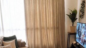 Un saló amb un sofà, una televisió sobre un moble, una planta i una finestra gran amb cortines.