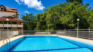 Una piscina rectangular amb una terrassa enrajolada, envoltada per una tanca de metall blanc i arbres al fons.