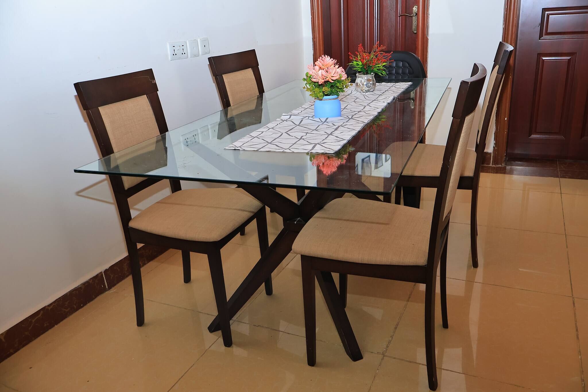 Une table à manger avec un plateau en verre, entourée de quatre chaises dotées d’assises et de dossiers rembourrés.