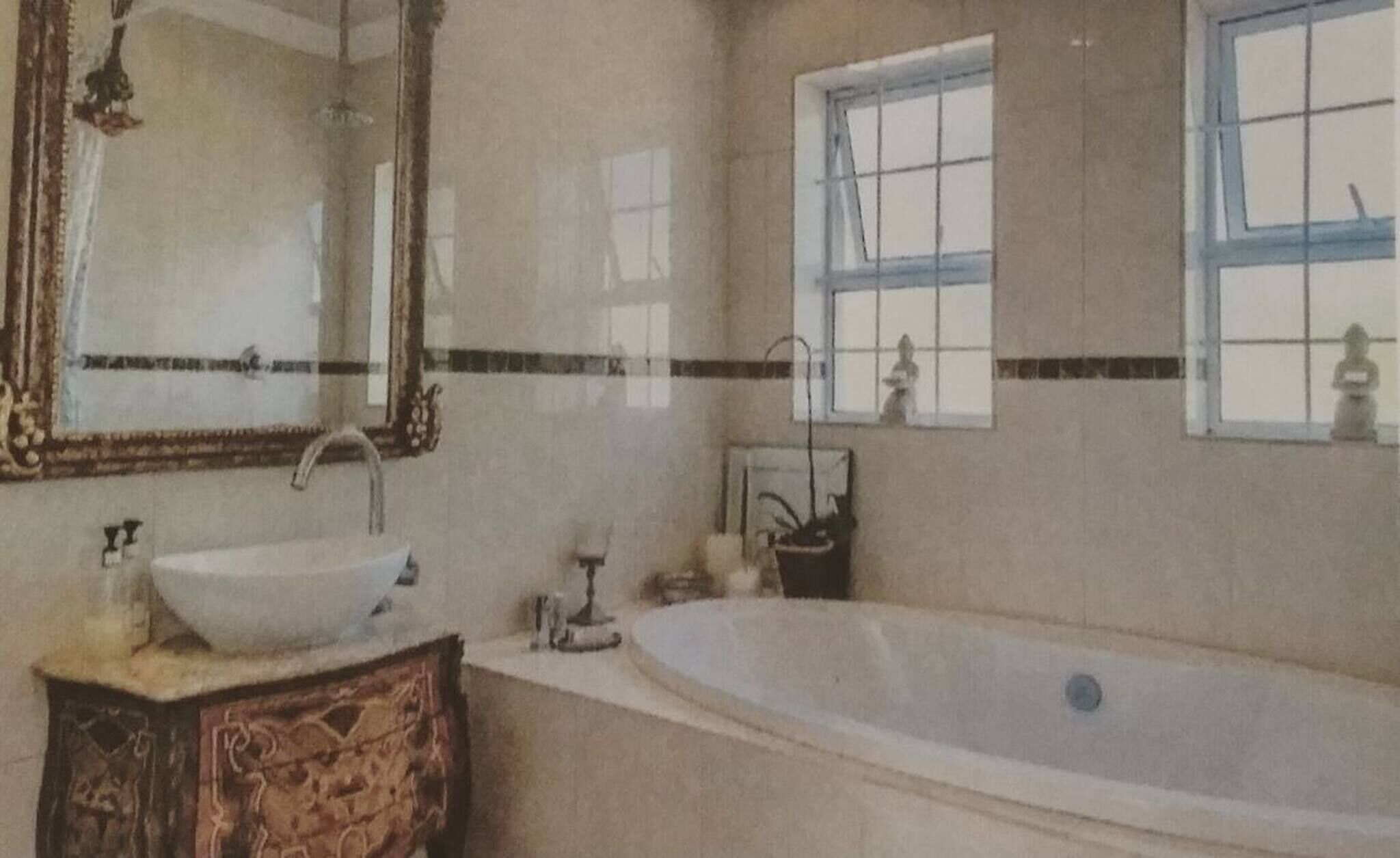A bathroom with a large mirror, a sink, a bathtub, and two windows.