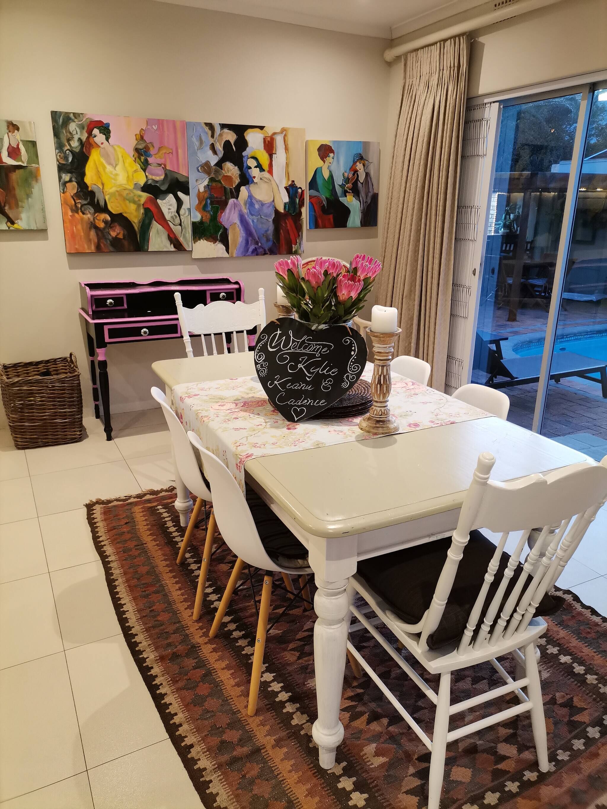 Een eetgedeelte met een tafel gedekt voor vier personen, omringd door witte stoelen met zwarte kussens. Op de tafel staat een zwarte vaas met roze bloemen en een kandelaar.